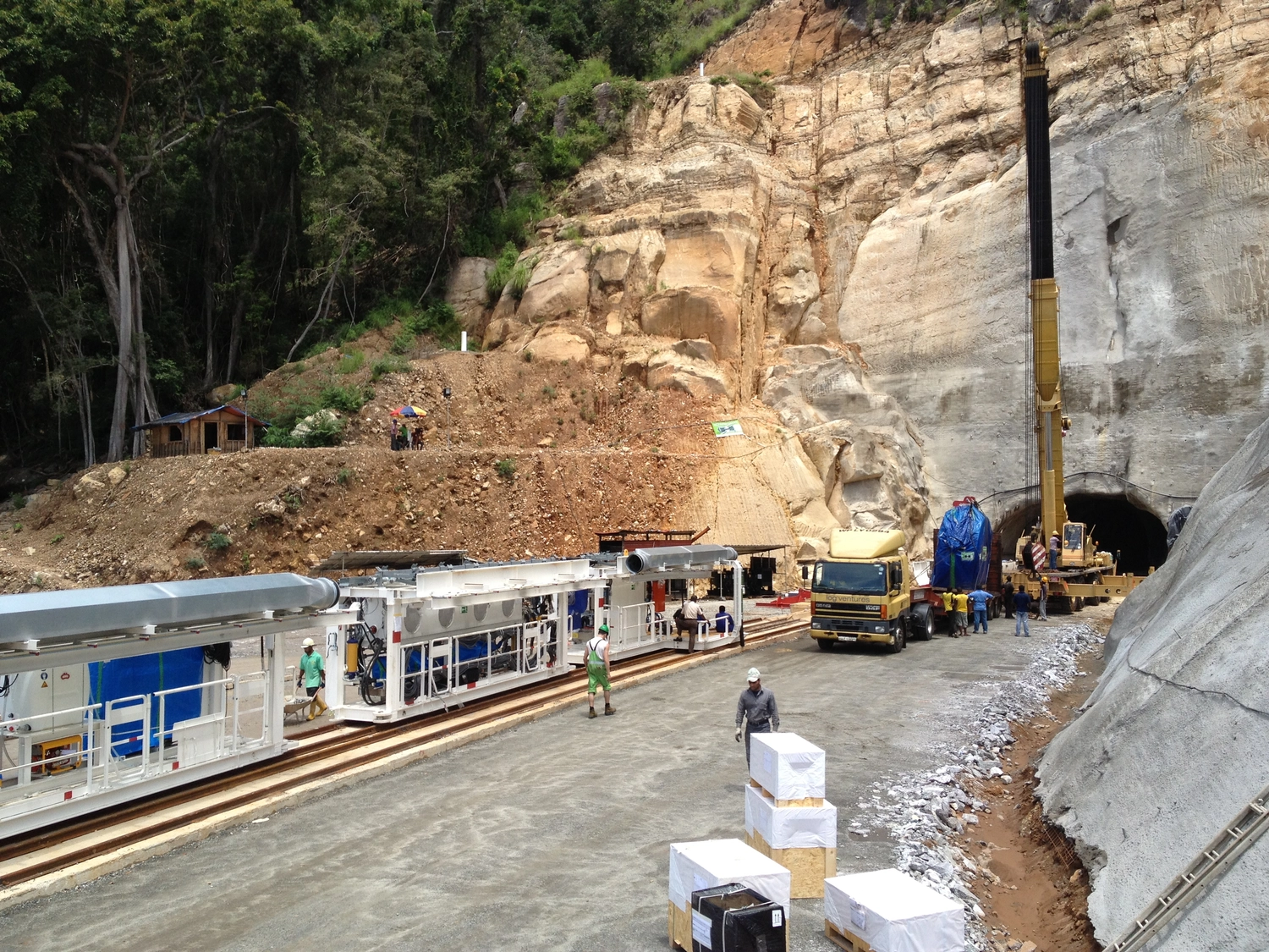 Dr. Rehm – Tunnelbau-Service – Eine Baustelle an einem Tunneleingang mit Arbeitern, schwerem Gerät und einem Lkw mit großem Baugerät.
